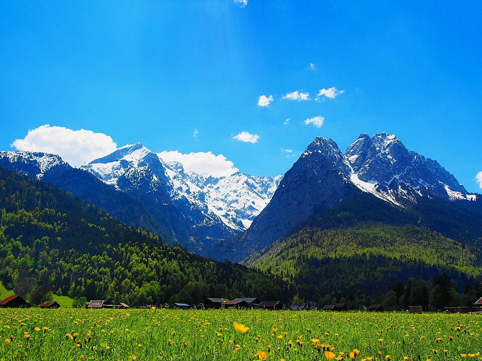 Snow-streaked peaks of the Zugspitze massif above green Alpine meadows.